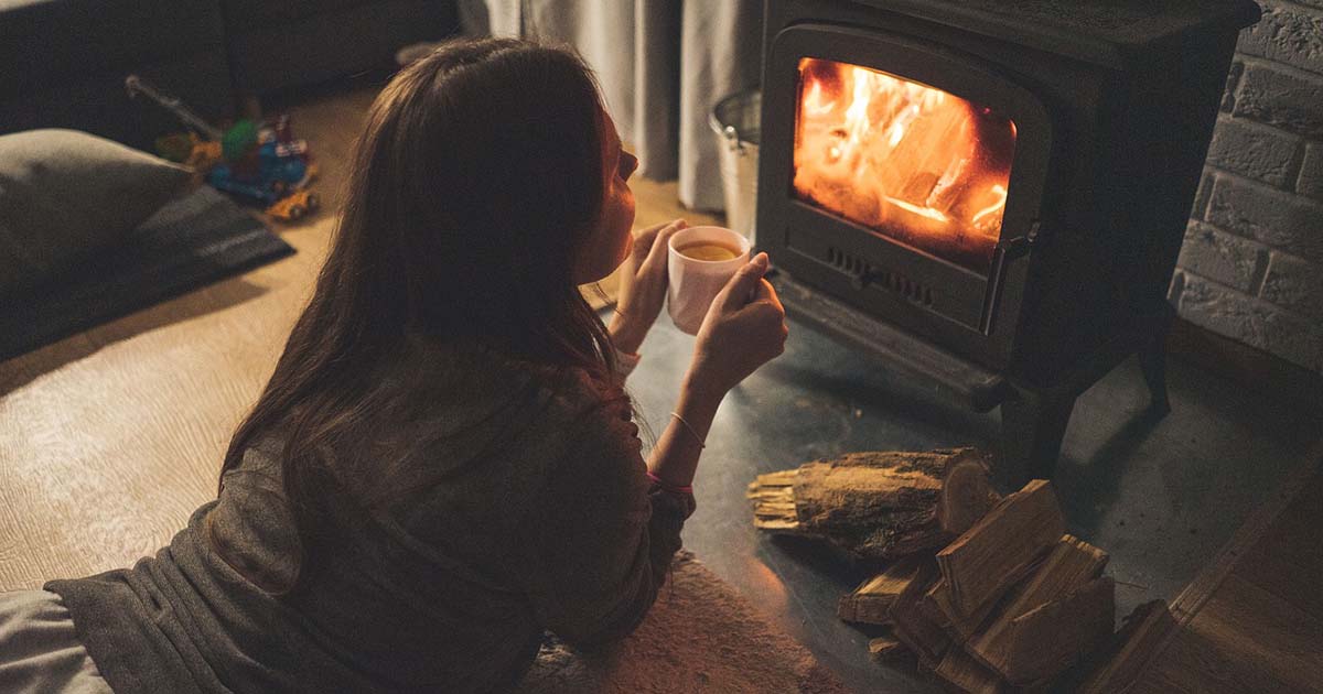Frau am Kamin nimmt sich eine Auszeit mit einer Tasse Tee