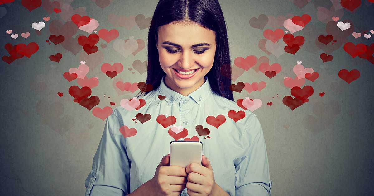 Junge Frau liest lächelnd eine Nachricht auf dem Smartphone – Online-Dating mit Herzsymbolen