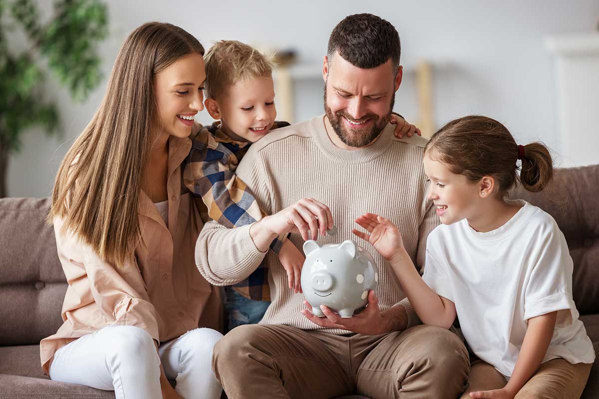 Glückliche Familie legt Geld in ein Sparschwein – Symbol für finanzielle Entlastung durch Elterngeld und Kinderfreibetrag