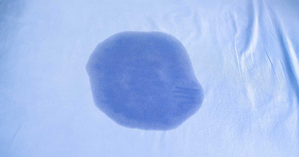 Urinfleck auf blauem Bettlaken als Symbol für nächtliches Einnässen bei Kindern