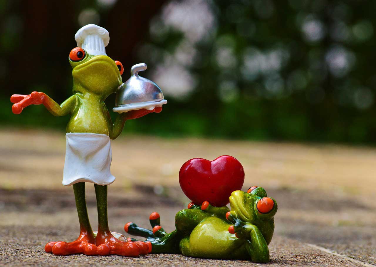 Zwei lustige Froschfiguren symbolisieren Liebe und gemeinsames Kochen – einer als Koch, der andere mit Herz.