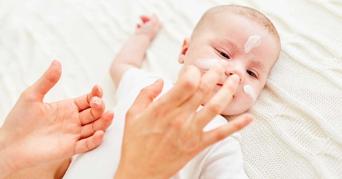 Mutter trägt einem Baby sanft Creme auf die empfindliche Gesichtshaut auf