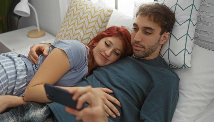 Paar liegt im Bett und schaut gemeinsam auf ein Smartphone – symbolisiert digitale Intimität und Nähe.