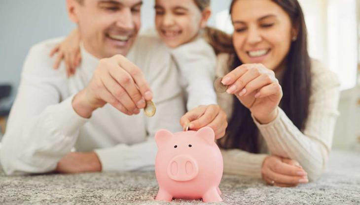 Familie wirft gemeinsam Geld in ein Sparschwein – Symbol für Finanzplanung im Familienalltag.