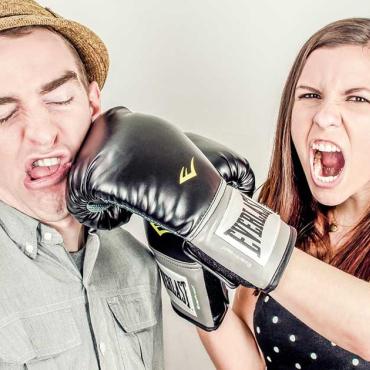 Frau mit Boxhandschuh schlägt Mann ins Gesicht – symbolischer Beziehungsstreit