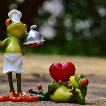 Zwei lustige Froschfiguren symbolisieren Liebe und gemeinsames Kochen – einer als Koch, der andere mit Herz.