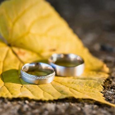 Zwei silberne Eheringe liegen auf einem gelben Herbstblatt auf Steinboden.