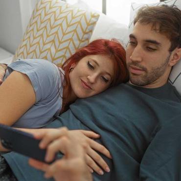 Paar liegt im Bett und schaut gemeinsam auf ein Smartphone – symbolisiert digitale Intimität und Nähe.