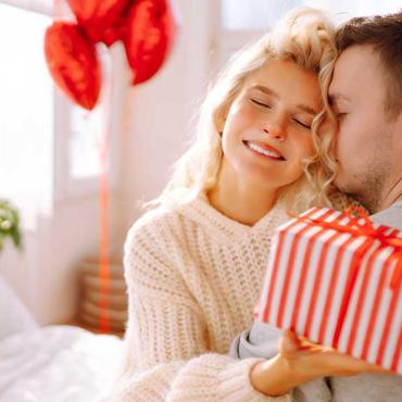 Frau umarmt Partner und überreicht ihm ein Geschenk als romantische Überraschung