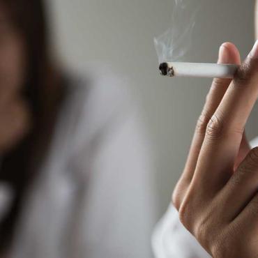 Mann raucht eine Zigarette, Partnerin im Hintergrund wirkt genervt und distanziert