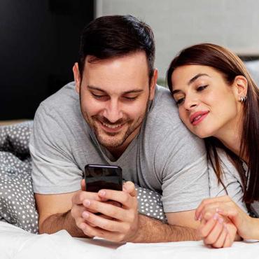 Paar schaut gemeinsam auf ein Smartphone im Bett