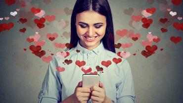 Junge Frau liest lächelnd eine Nachricht auf dem Smartphone – Online-Dating mit Herzsymbolen