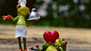 Zwei lustige Froschfiguren symbolisieren Liebe und gemeinsames Kochen – einer als Koch, der andere mit Herz.
