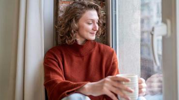 Frau genießt ruhigen Selfcare-Moment mit einer Tasse Tee am Fenster
