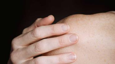 Person legt die Hand achtsam auf die eigene Schulter als Symbol für Selbstakzeptanz, Körperbewusstsein und Body Positivity
