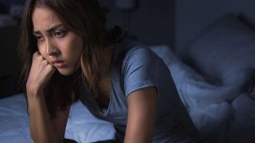 Trauernde Frau sitzt nachdenklich auf dem Bett und verarbeitet einen Verlust in der Familie