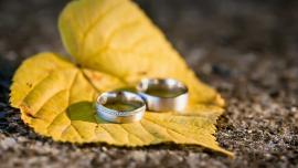 Zwei silberne Eheringe liegen auf einem gelben Herbstblatt auf Steinboden.