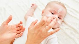Mutter trägt einem Baby sanft Creme auf die empfindliche Gesichtshaut auf