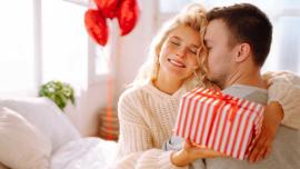 Frau umarmt Partner und überreicht ihm ein Geschenk als romantische Überraschung