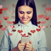 Junge Frau liest lächelnd eine Nachricht auf dem Smartphone – Online-Dating mit Herzsymbolen