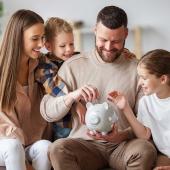 Glückliche Familie legt Geld in ein Sparschwein – Symbol für finanzielle Entlastung durch Elterngeld und Kinderfreibetrag