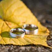 Zwei silberne Eheringe liegen auf einem gelben Herbstblatt auf Steinboden.