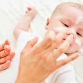 Mutter trägt einem Baby sanft Creme auf die empfindliche Gesichtshaut auf