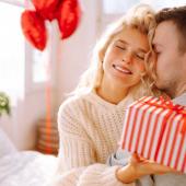 Frau umarmt Partner und überreicht ihm ein Geschenk als romantische Überraschung