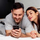 Paar schaut gemeinsam auf ein Smartphone im Bett