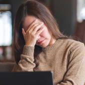 Frau mit Kopfdruck bei der Arbeit am Laptop
