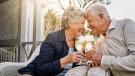 Älteres Ehepaar stößt mit Sektgläsern an und feiert gemeinsam auf der Terrasse ihre Goldene Hochzeit – beide lächeln sich liebevoll an.