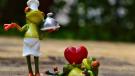 Zwei lustige Froschfiguren symbolisieren Liebe und gemeinsames Kochen – einer als Koch, der andere mit Herz.