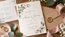 Elegante Hochzeitseinladung mit floralen Motiven, Eheringen, Umschlägen und rosafarbenem Seidenband auf einem Holztisch.
